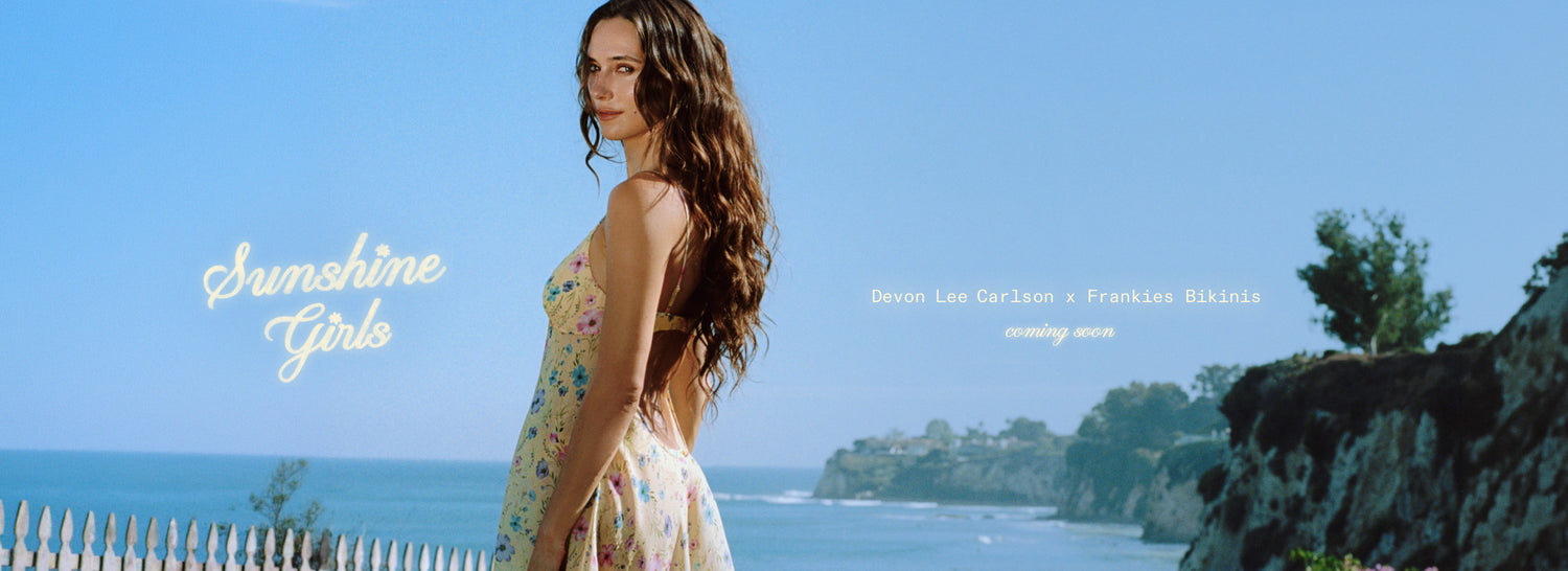 Devon wearing a floral sleeveless dress stands by the ocean with cliffs and blue sky in the background. The words 'Sunshine Girls' appear on the left, with song text on the right.
